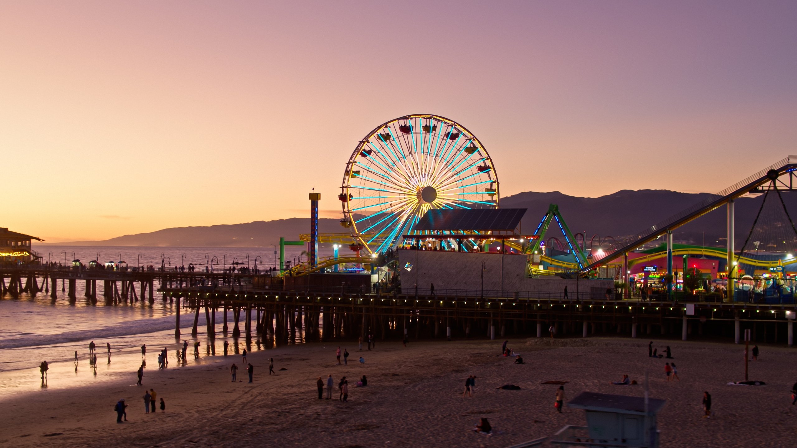 Aerial view of the Santa Monica Pier with a ferris wheel lit up and the sun setting behind it