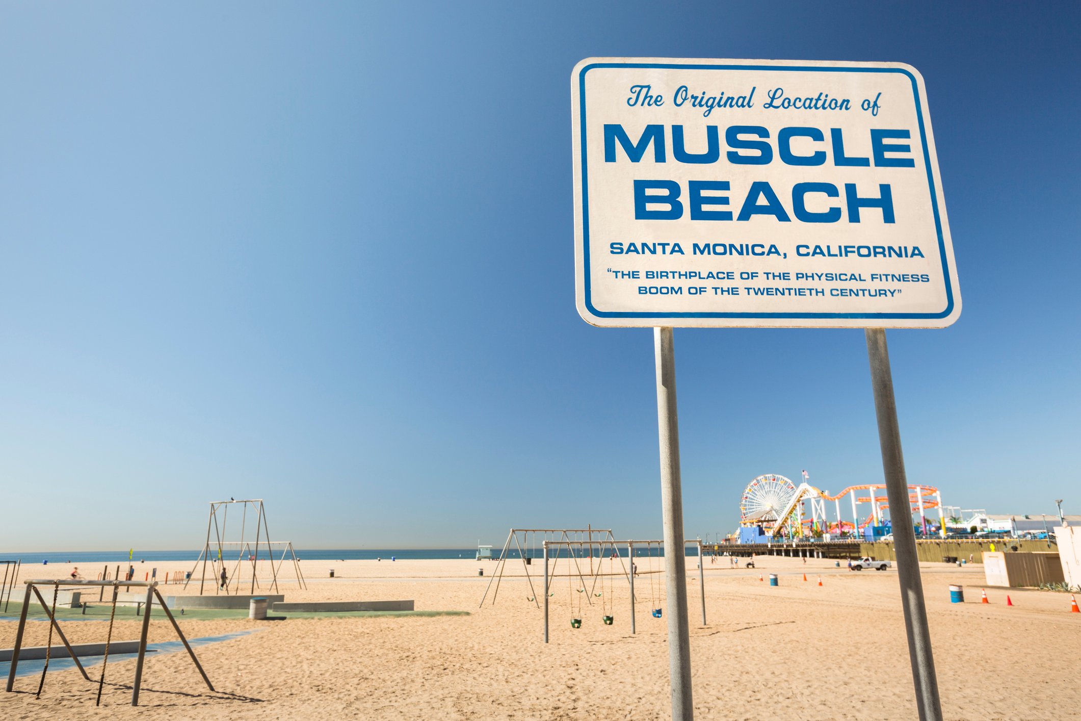 Muscle Beach sign with the beach and santa monica pier in the background