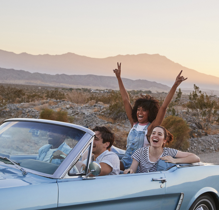 a group of friends driving in a car while someone in the back holds up peace signs