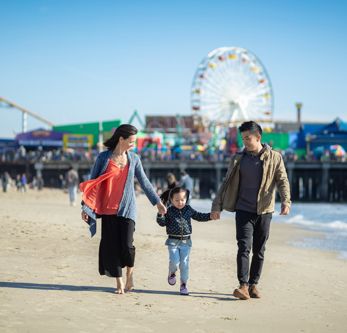 A family walking on the beach with the Santa Monica Pier in the background