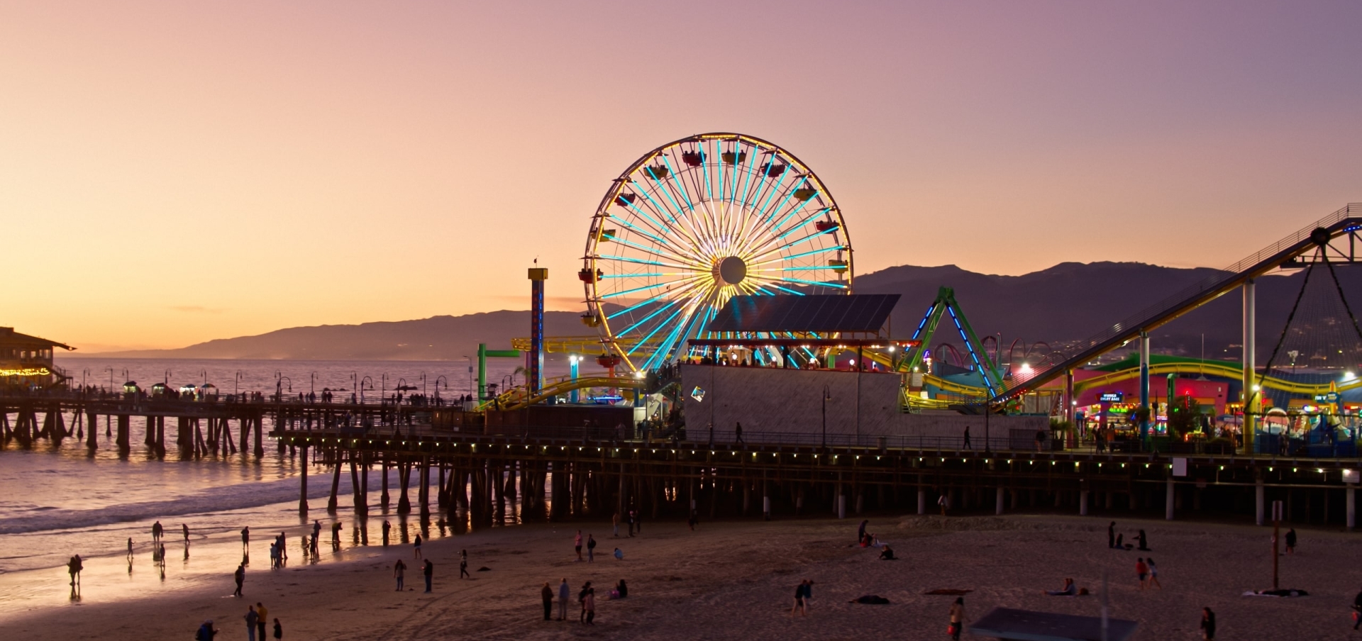 Aerial view of the Santa Monica Pier with a ferris wheel lit up and the sun setting behind it