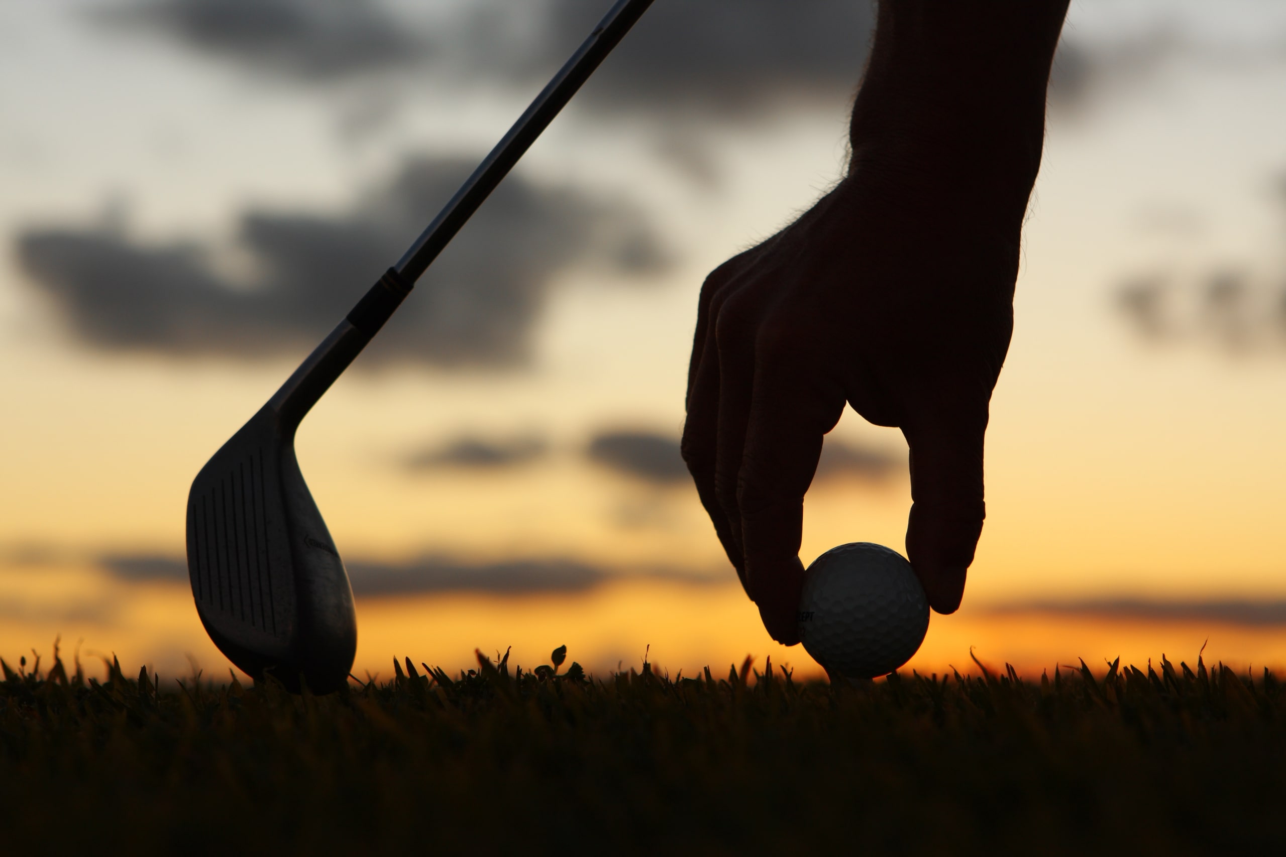 someone setting up a golf ball on a tee with the sun setting in the background